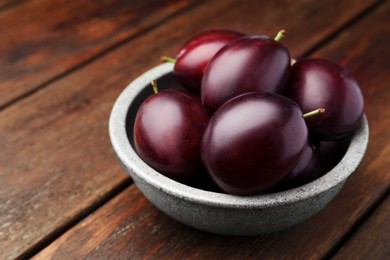 Photo of Tasty ripe plums in bowl on wooden table