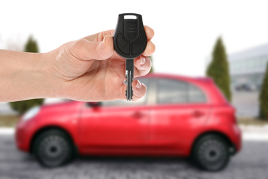 Image of Car buying. Woman holding key against blurred automobile, closeup