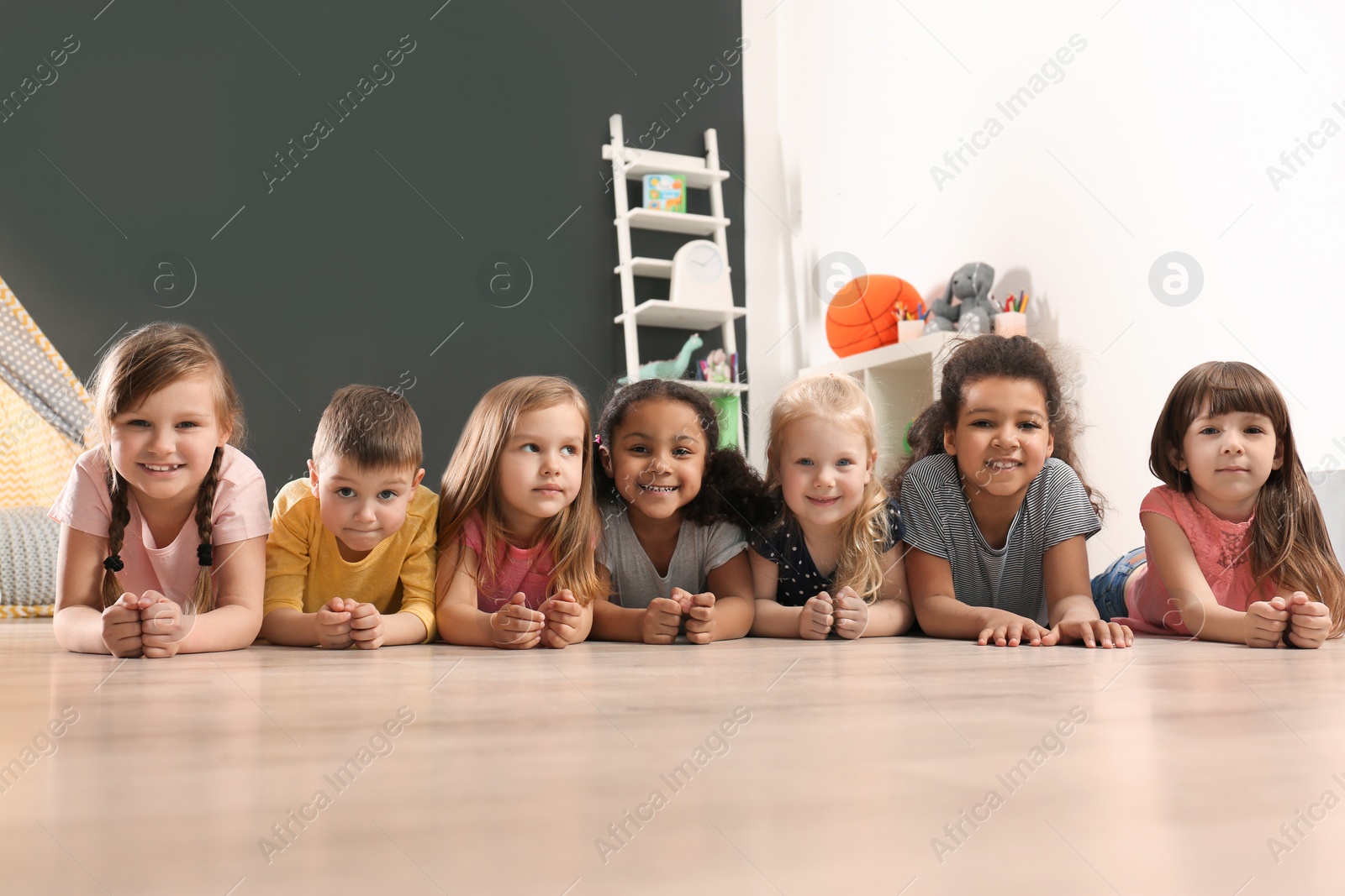 Photo of Cute little children lying on floor in kindergarten. Indoor activity