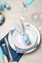 Photo of Festive table setting with bunny ears made of light blue egg and napkin, above view. Easter celebration