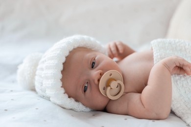 Photo of Cute newborn baby in white knitted hat lying on bed