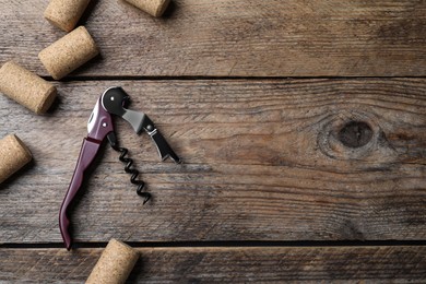 Photo of Corkscrew and wine corks on wooden table, flat lay. Space for text