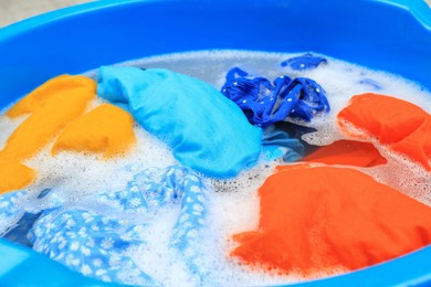 Photo of Basin with colorful clothes in suds, closeup. Hand washing laundry