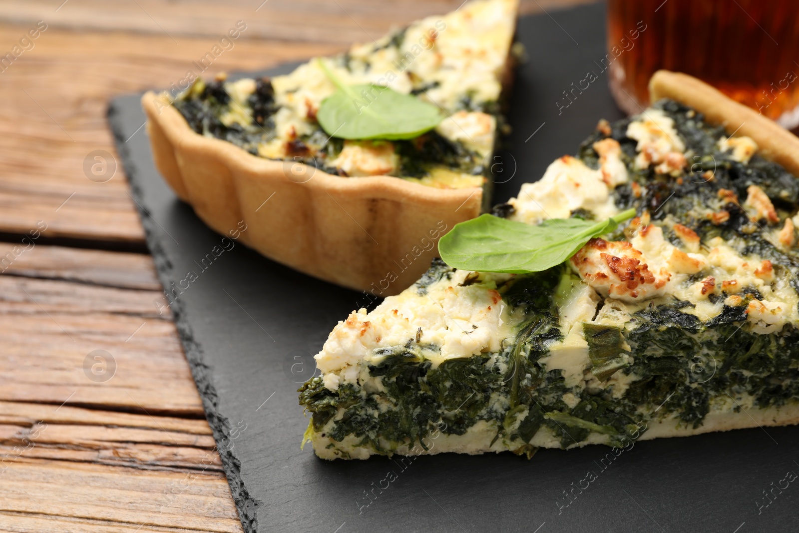 Photo of Pieces of delicious homemade spinach quiche on black board, closeup