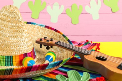 Mexican sombrero hat, ukulele and maracas on yellow table, closeup
