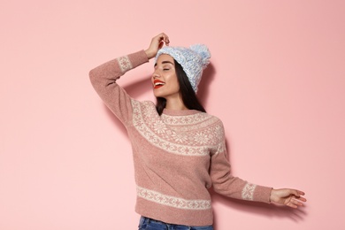 Young woman in warm sweater and knitted hat on color background. Celebrating Christmas