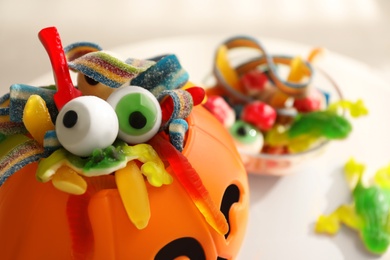 Photo of Halloween trick or treat bucket and many different sweets on white table, closeup