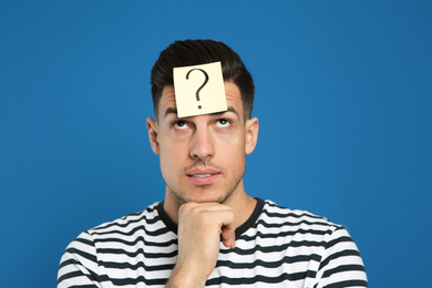 Photo of Pensive man with question mark sticker on forehead against blue background