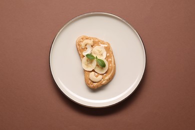 Photo of Toast with tasty nut butter, banana slices and cashews on brown background, top view