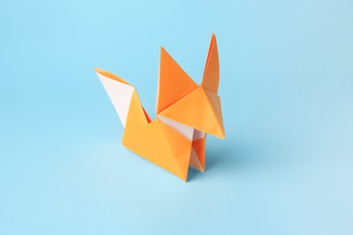 Photo of Origami art. Handmade orange paper fox on light blue background