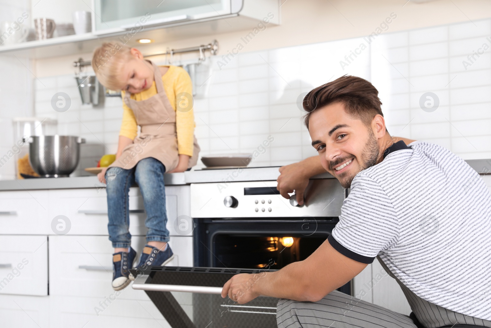 Photo of Young man and his son baking something in oven at home