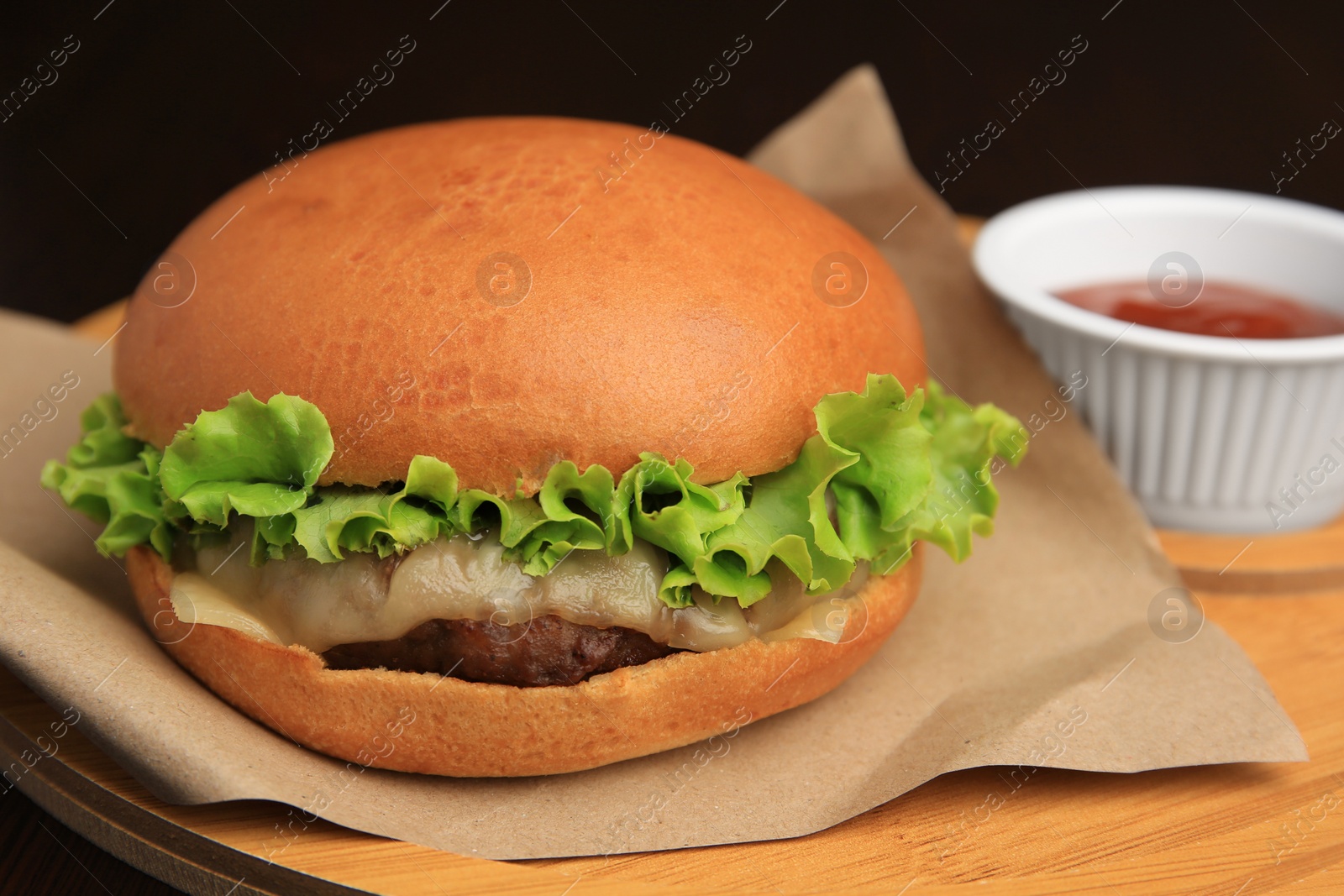 Photo of Tasty cheeseburger and sauce on wooden board, closeup
