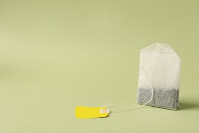 Photo of Paper tea bag with tag on light green background, space for text