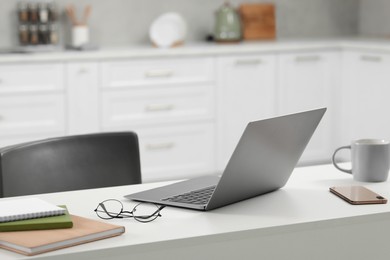 Photo of Home office. Laptop, glasses, smartphone and stationery on white desk in kitchen