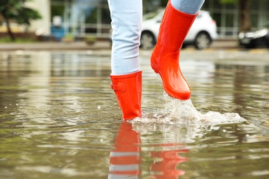 Photo of Woman with red rubber boots in puddle, closeup. Rainy weather