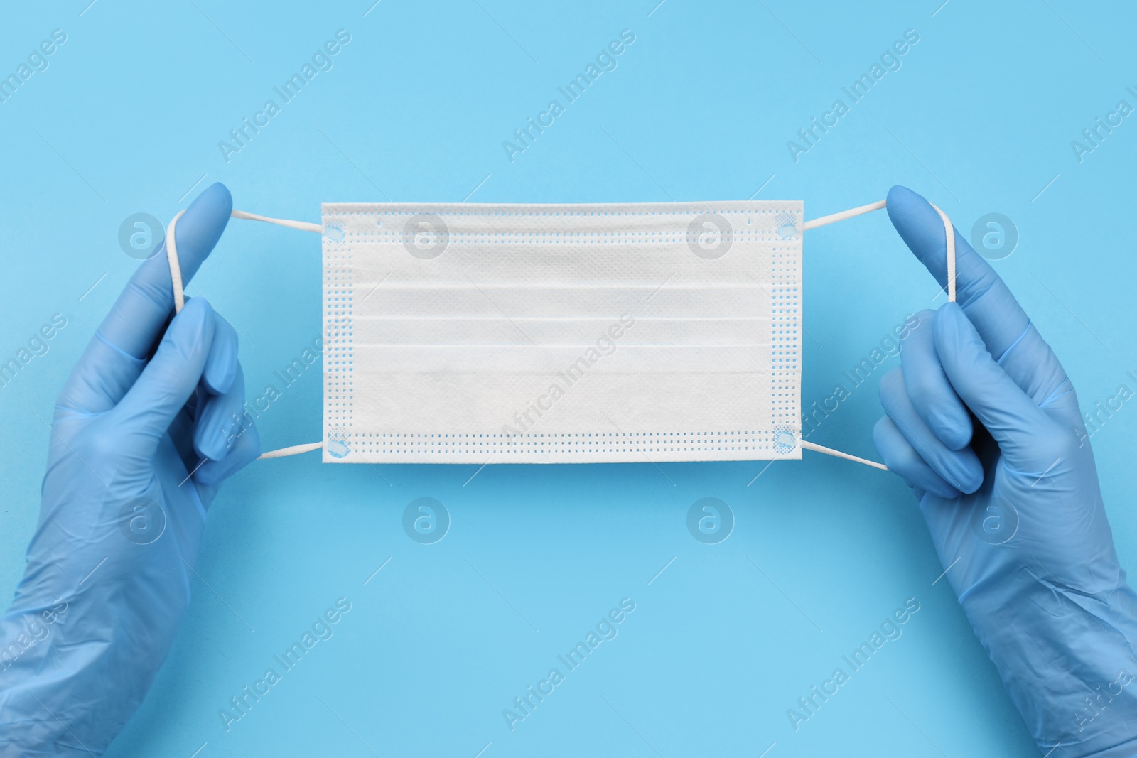 Photo of Doctor in medical gloves holding protective mask on light blue background, closeup