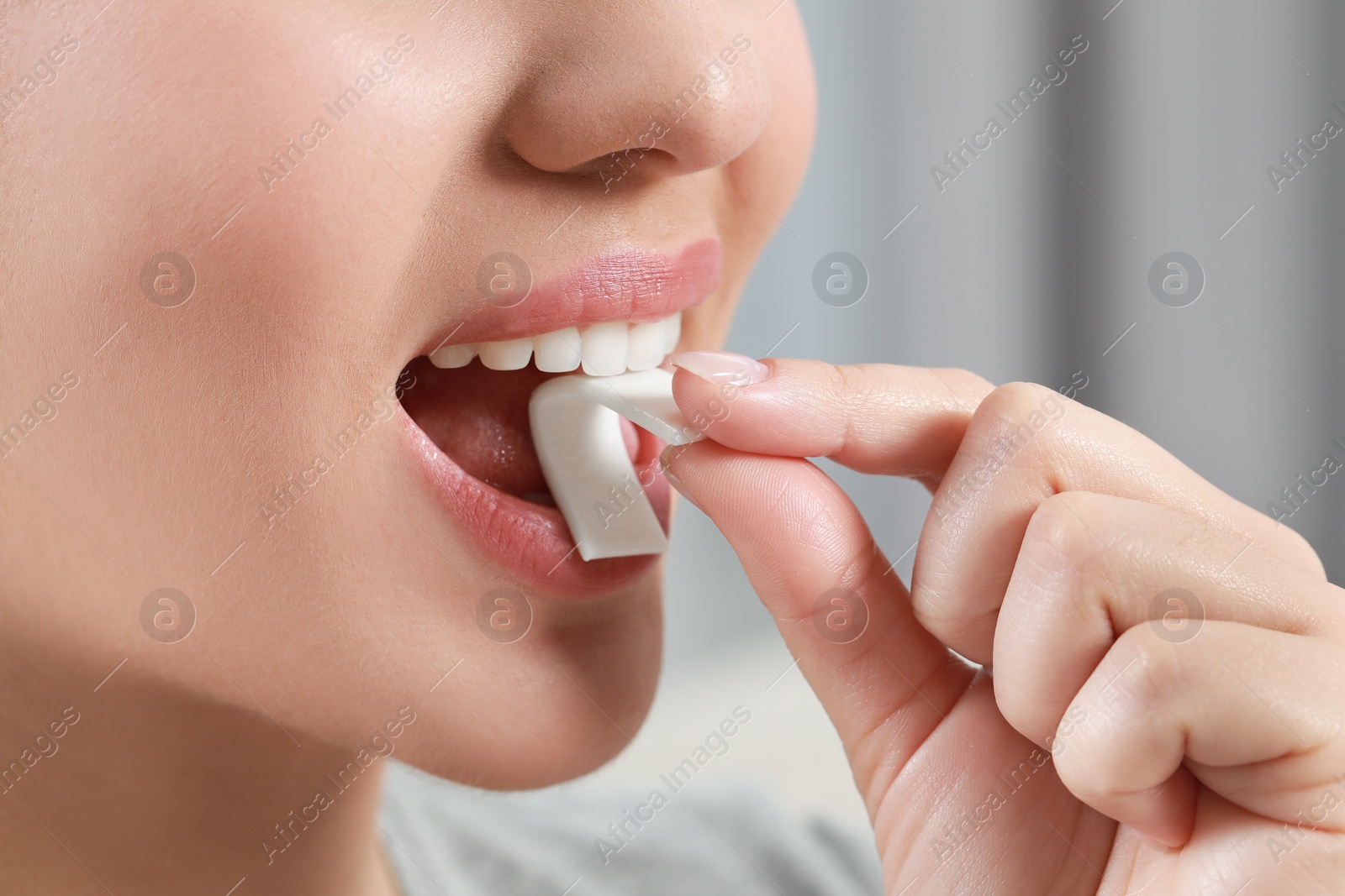 Photo of Woman putting chewing gum piece into mouth on blurred background, closeup