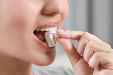 Photo of Woman putting chewing gum piece into mouth on blurred background, closeup