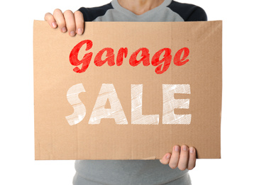 Woman holding piece of cardboard with phrase GARAGE SALE on white background, closeup
