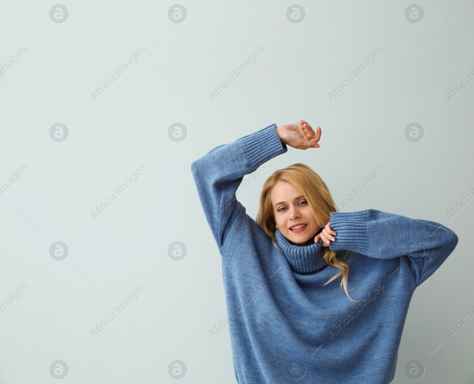 Photo of Beautiful young woman wearing warm blue sweater on light background. Space for text