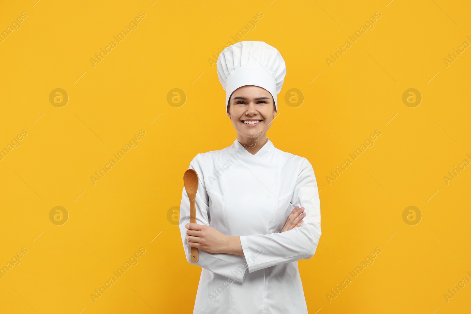 Photo of Happy female chef with wooden spoon on orange background