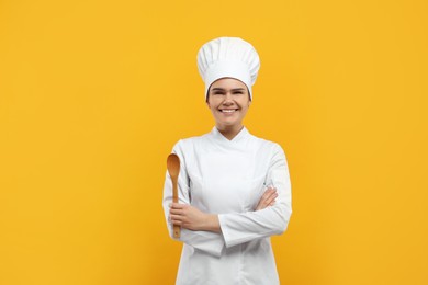 Photo of Happy female chef with wooden spoon on orange background
