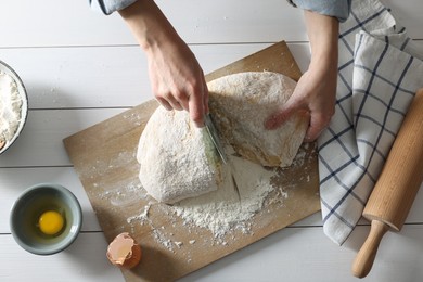 Woman cutting dough at white wooden table, top view