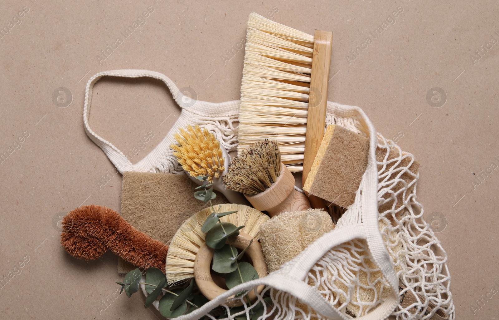 Photo of Cleaning brushes, sponges, eucalyptus leaves and string bag on pale brown background, top view