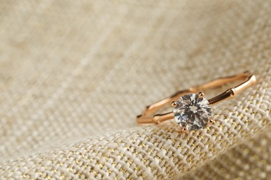 Photo of Beautiful engagement ring on sack fabric, closeup. Space for text