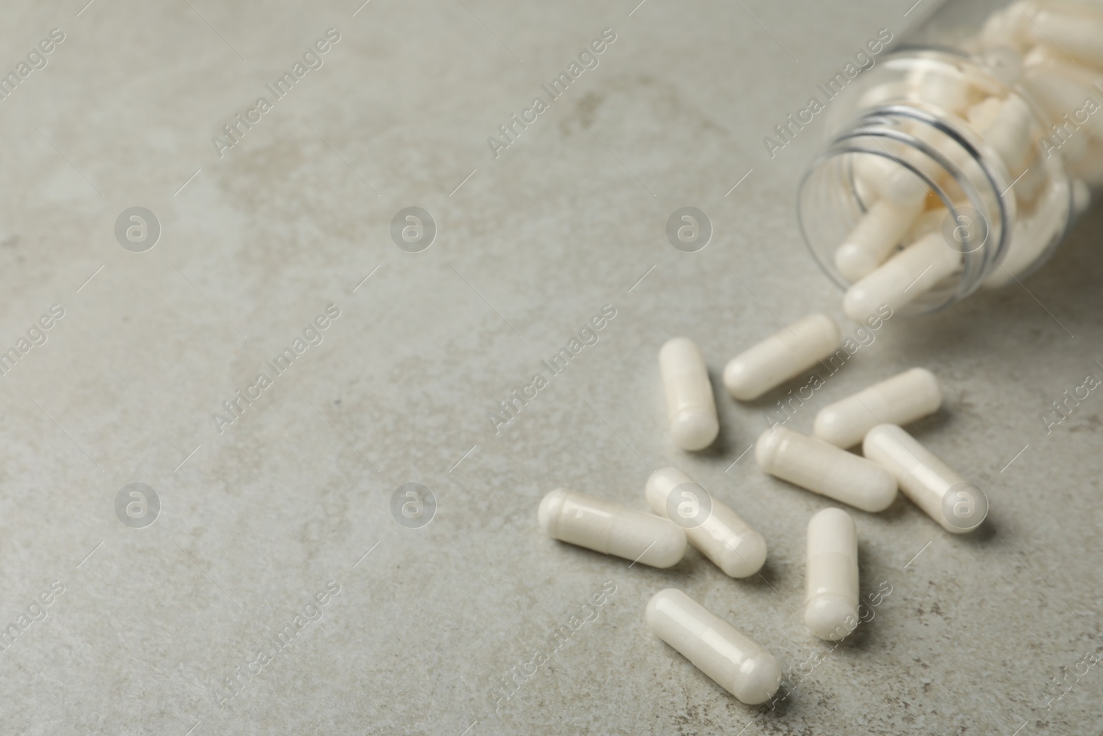 Photo of Overturned bottle with dietary supplement capsules on light grey table. Space for text