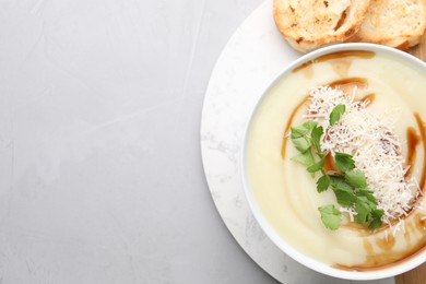 Delicious cream soup with parmesan cheese, soy sauce in bowl and croutons on light grey table, flat lay. Space for text