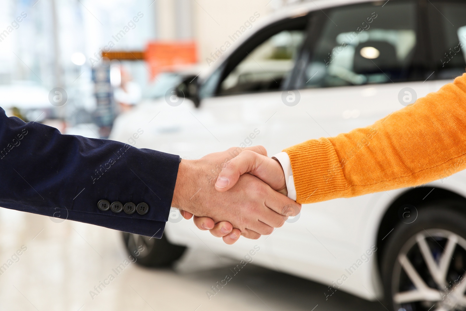 Photo of Salesman shaking hands with client in car dealership, closeup