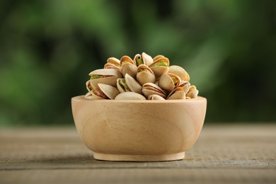 Photo of Tasty pistachios in bowl on wooden table against blurred background, closeup