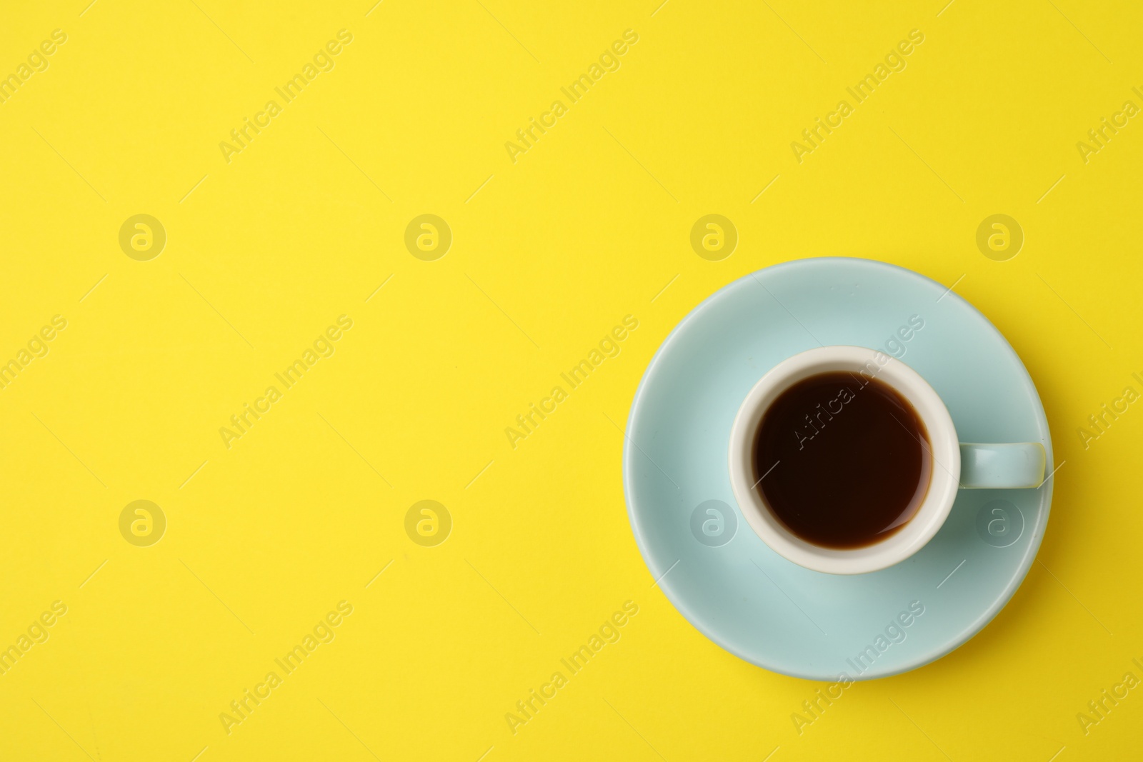 Photo of Tasty coffee in cup on yellow background, top view. Space for text