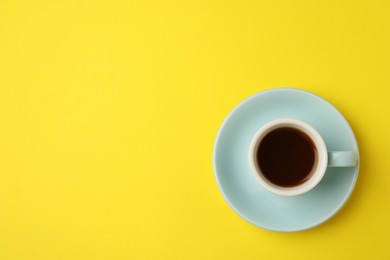 Tasty coffee in cup on yellow background, top view. Space for text