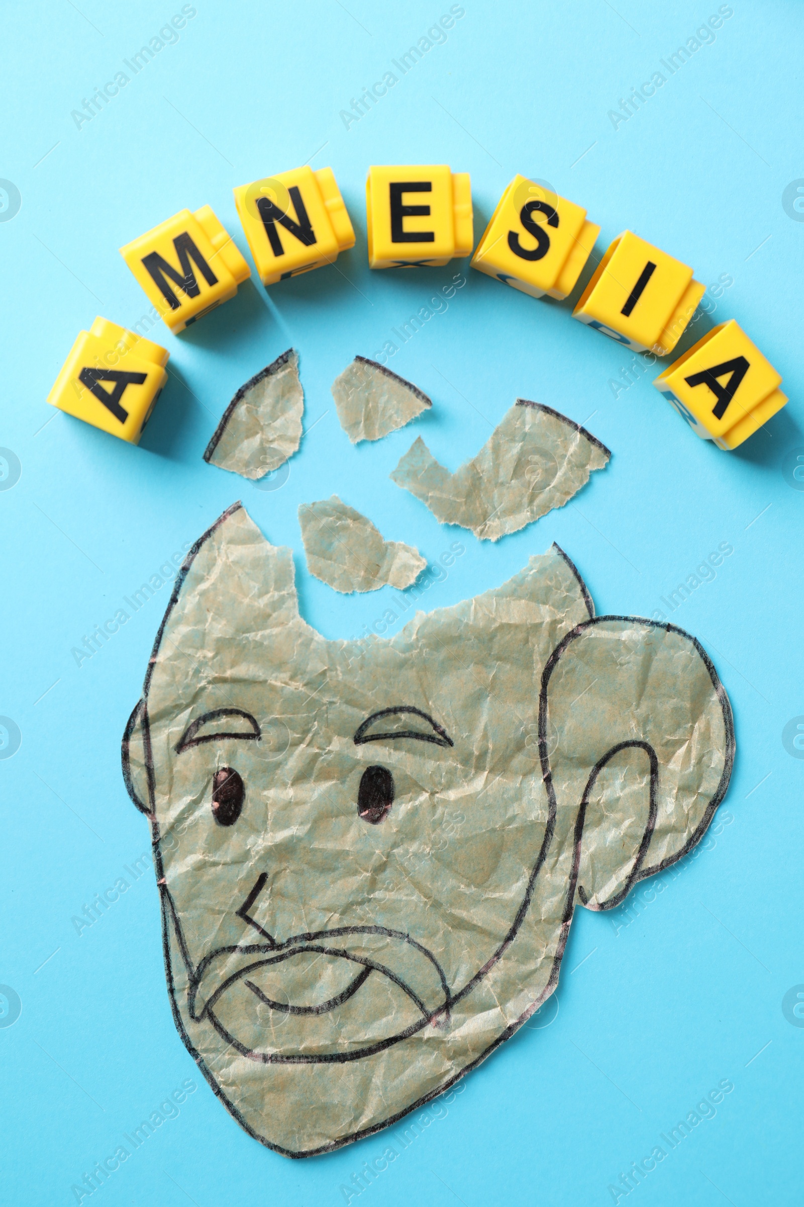 Photo of Yellow cubes with word Amnesia and human head with brain pieces made of crumbled paper on light blue background, flat lay