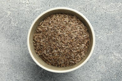 Photo of Bowl of dry dill seeds on grey table, top view