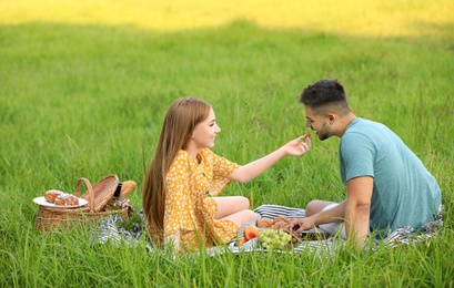 Photo of Young woman feeding her boyfriend with grape at picnic outdoors