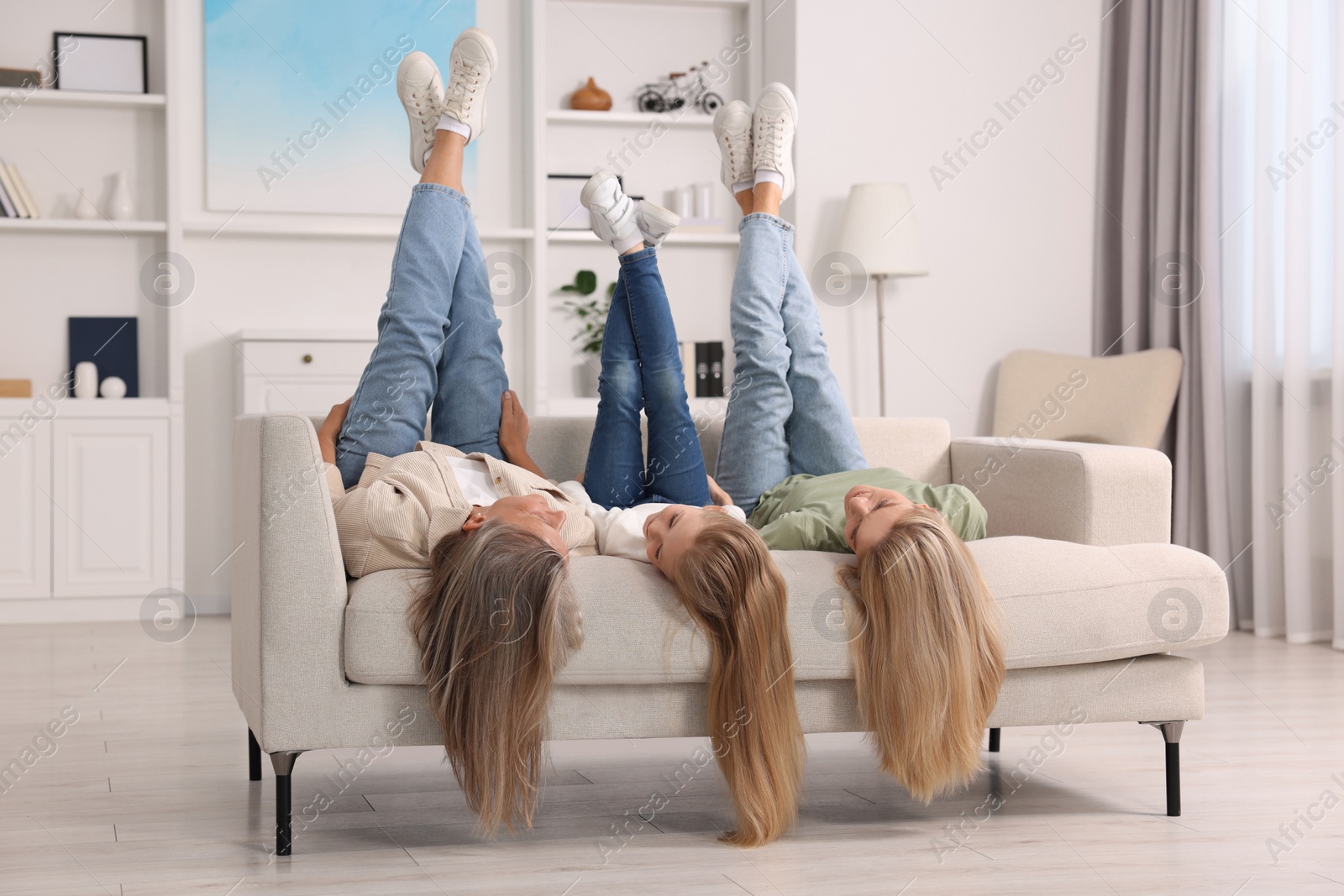 Photo of Three generations. Grandmother, her daughter and granddaughter lying on couch at home