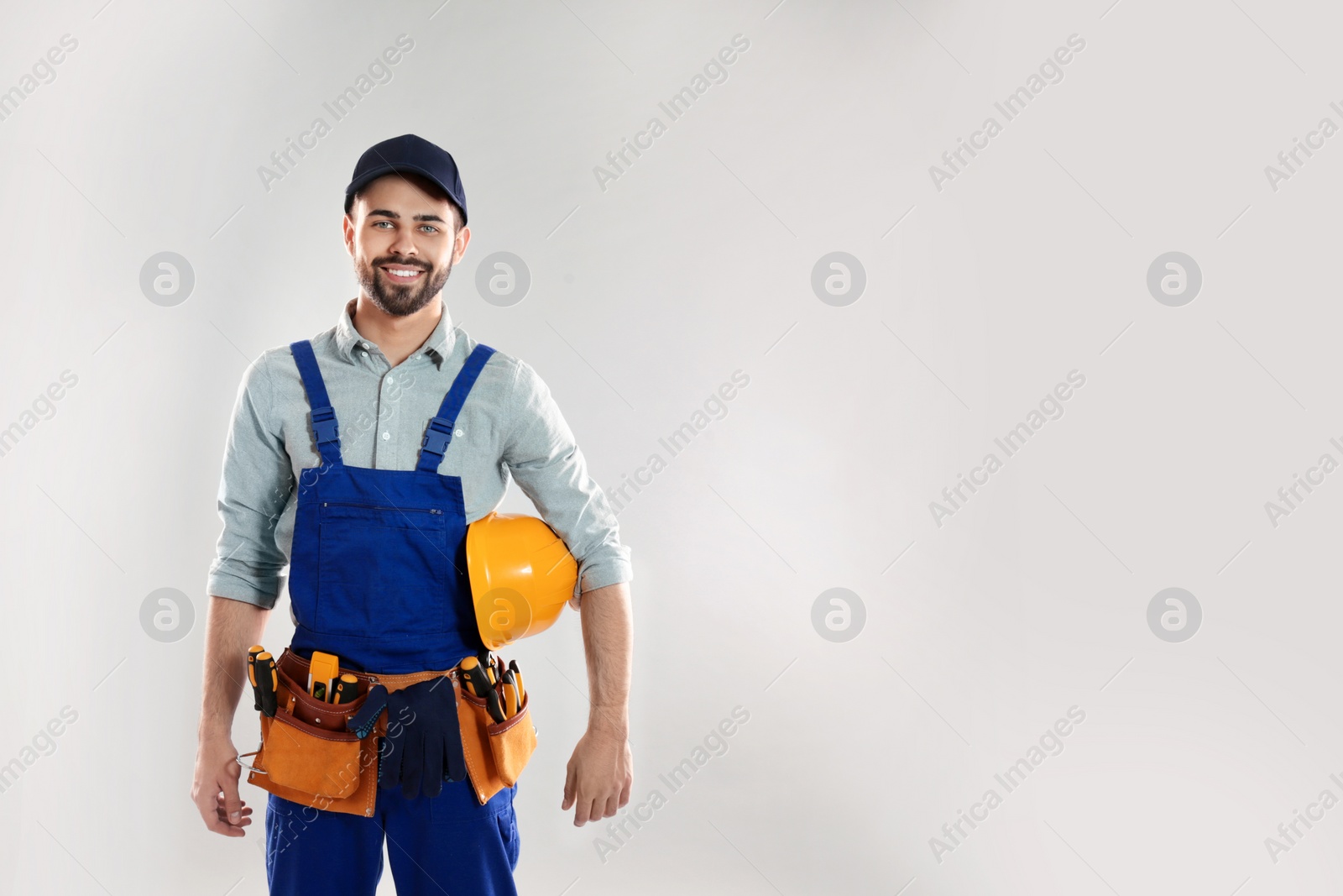 Photo of Portrait of construction worker with hard hat and tool belt on light background, space for text