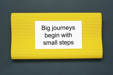 Card with phrase Big Journeys Begin With Small Steps on dark background, top view. Motivational quote