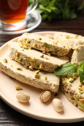 Photo of Pieces of tasty halva with pistachios and mint on table, closeup