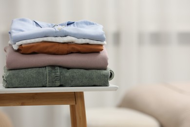 Photo of Stack of different folded clothes on bedside table indoors, closeup. Space for text
