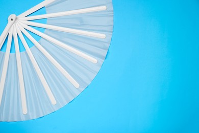Photo of Stylish white hand fan on light blue background, top view. Space for text