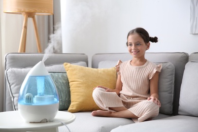 Photo of Little girl on sofa in room with modern air humidifier