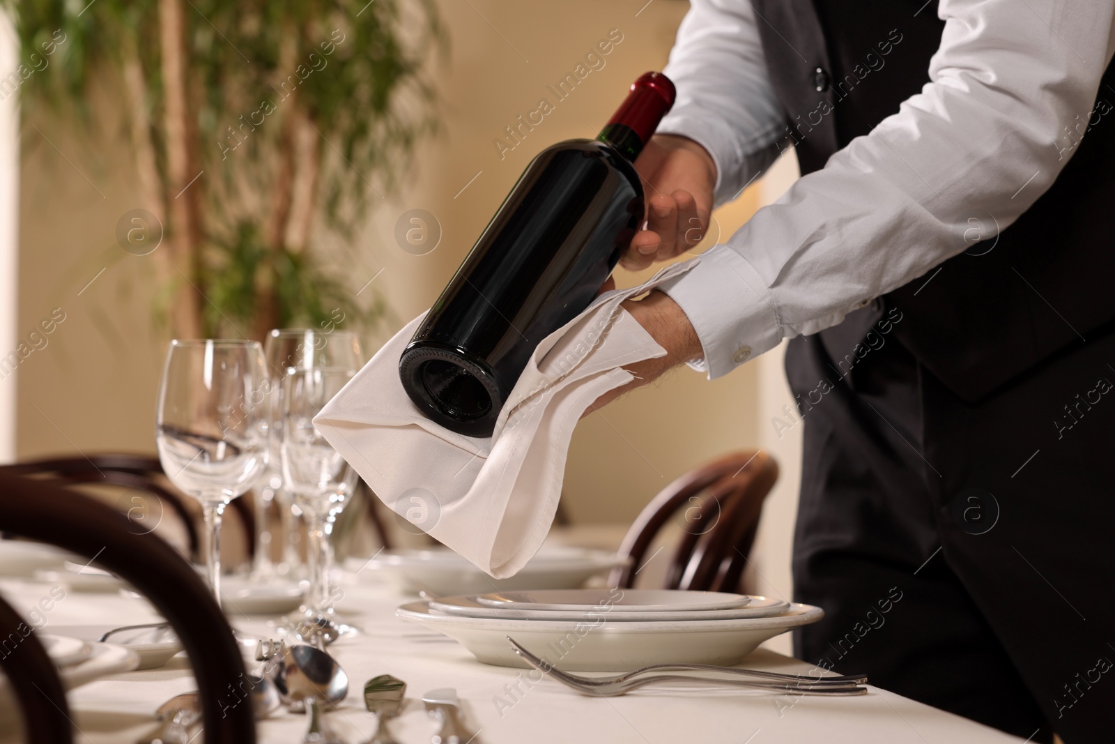 Photo of Butler holding bottle of wine near table in restaurant, closeup