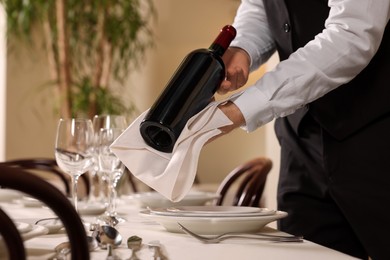 Photo of Butler holding bottle of wine near table in restaurant, closeup