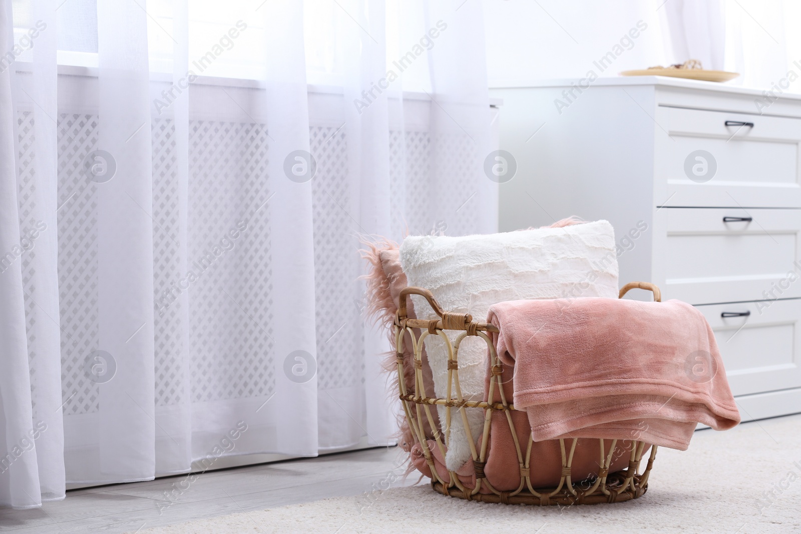 Photo of Basket with soft plaid and pillows in modern room interior