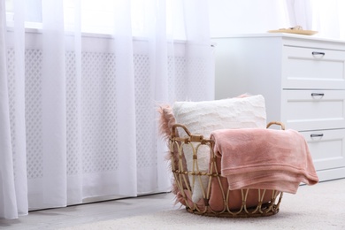 Basket with soft plaid and pillows in modern room interior