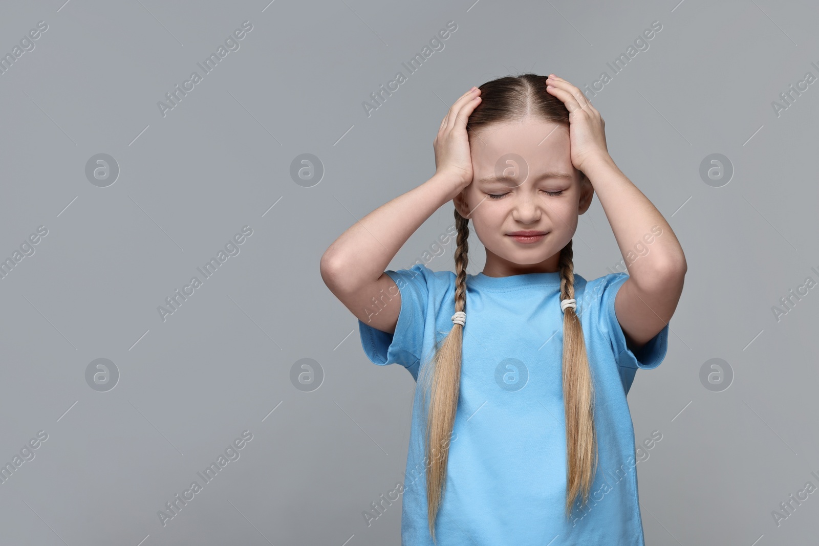 Photo of Little girl suffering from headache on grey background. Space for text